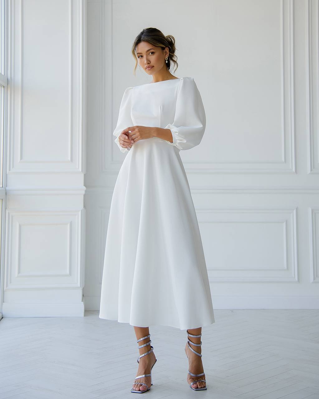 Woman wearing a white dress with long sleeves against a white wall