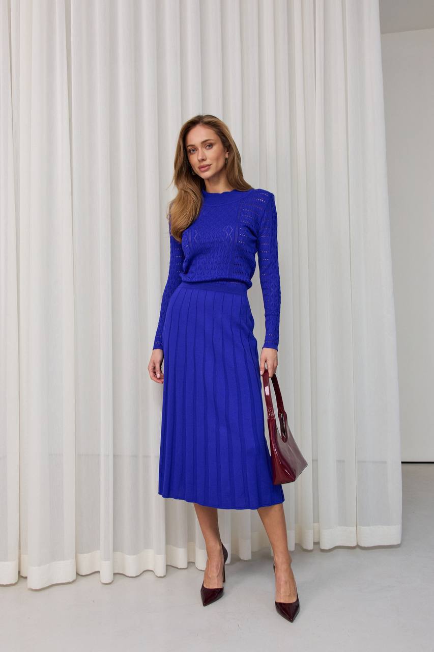 Woman wearing a blue outfit standing in front of white curtains