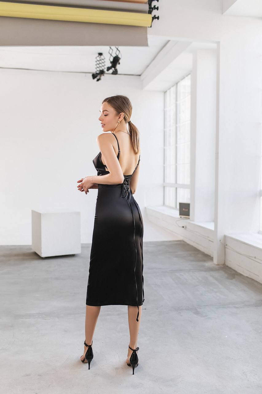 Woman in a black dress standing in a modern indoor setting with white walls and gray floor.