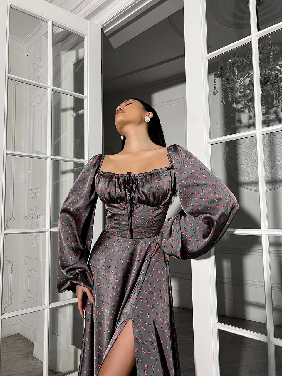 Woman in a floral dress standing in a room with large windows.