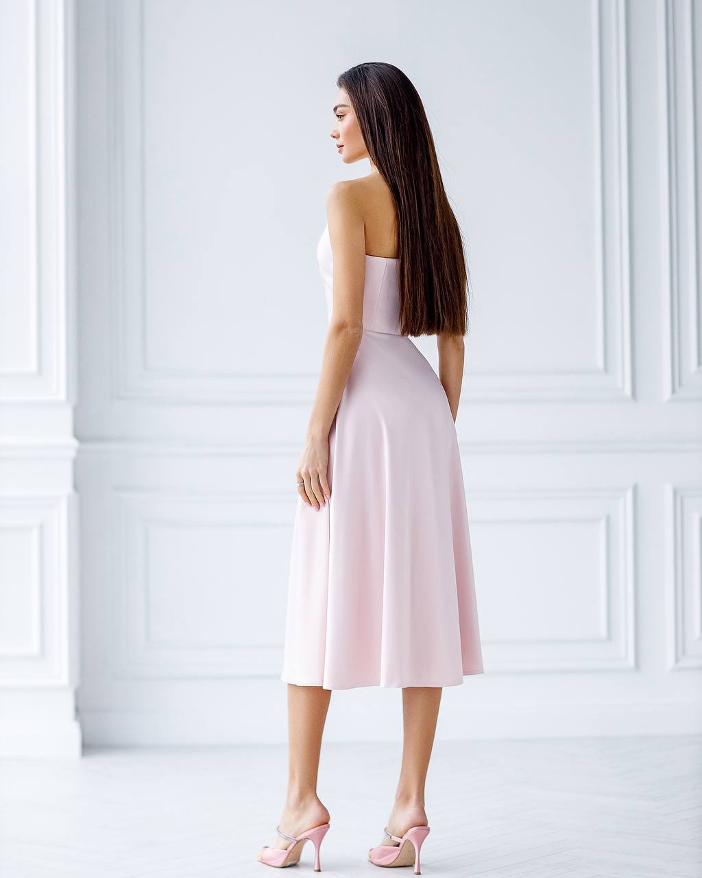 Woman wearing a light pink strapless dress against a white wall