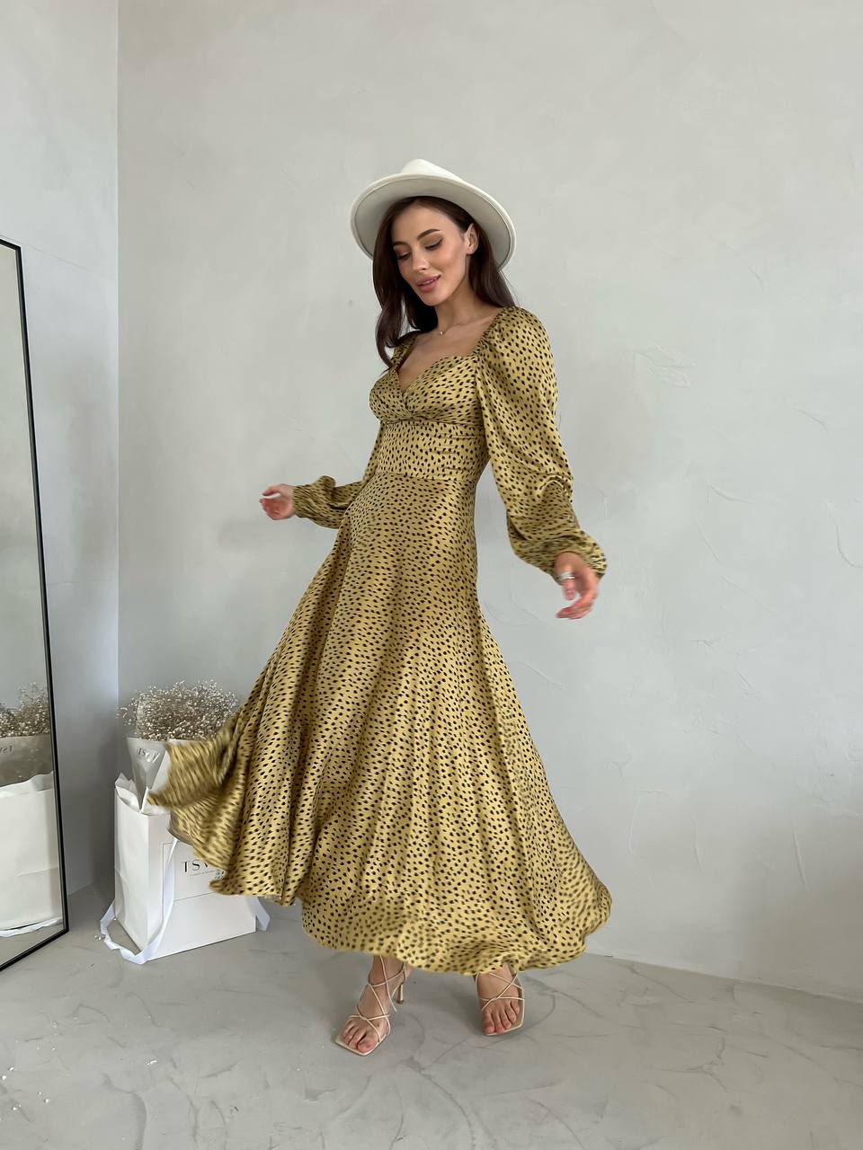 Woman wearing a gold dress with long sleeves and a white hat indoors.