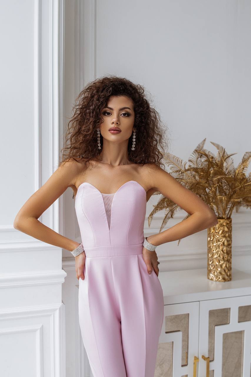 Woman wearing a pink strapless jumpsuit in an elegant interior setting.