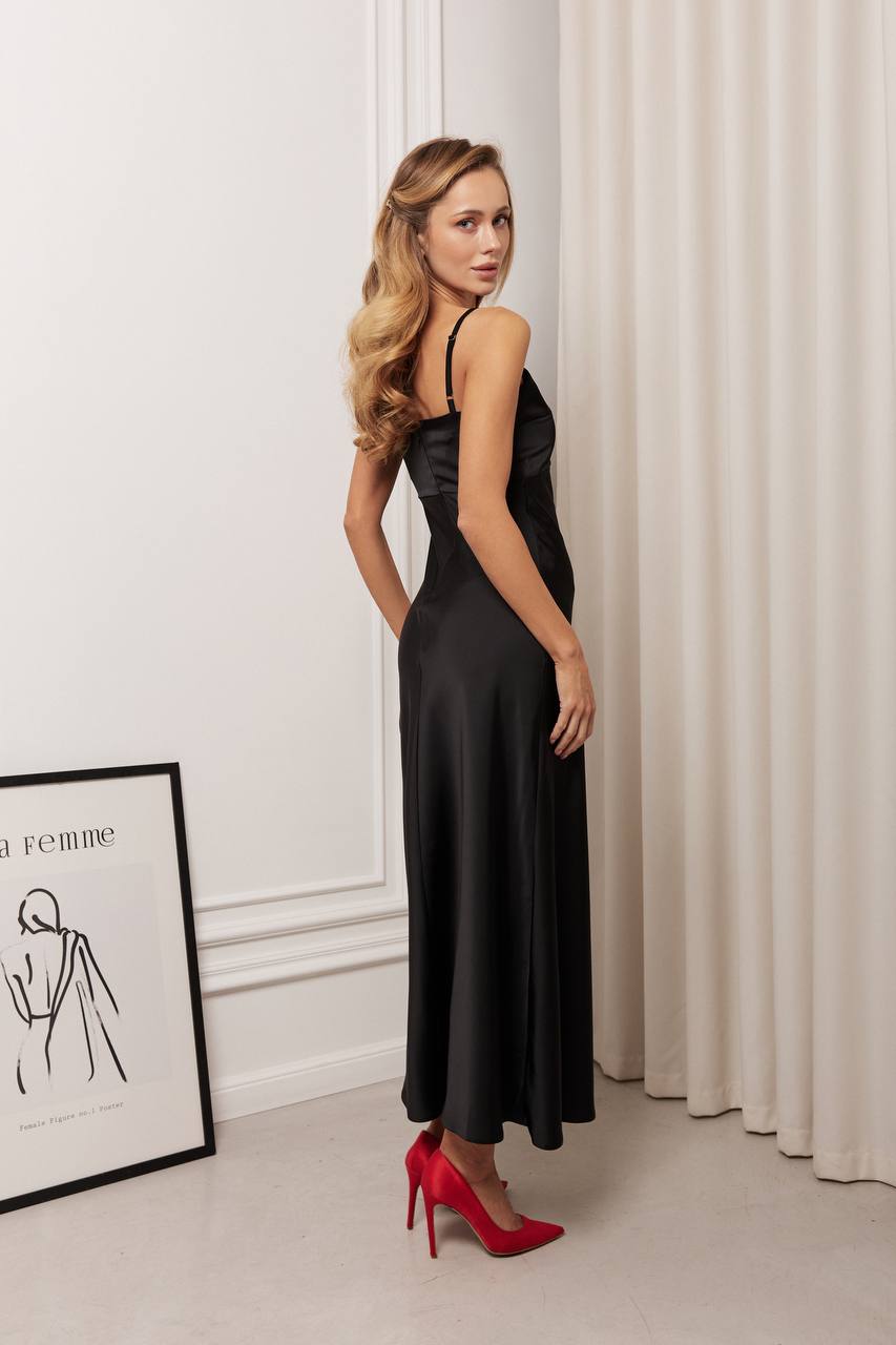 Woman in a black dress with red high heels standing in a room with white walls and curtains.