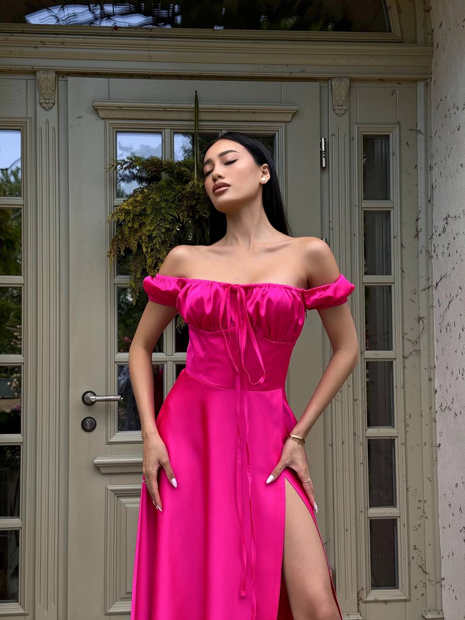 Woman in a bright pink off-shoulder dress standing in front of a door.