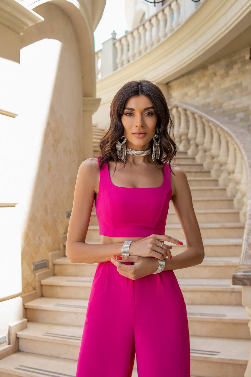 Woman in a bright pink outfit standing on a staircase with classical architecture.