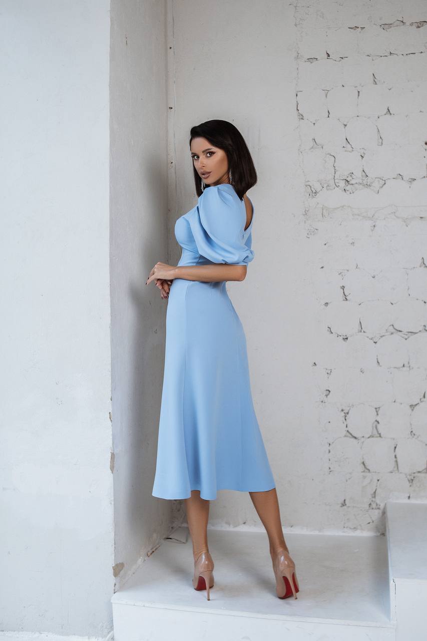 Woman in a light blue dress standing against a textured white wall.