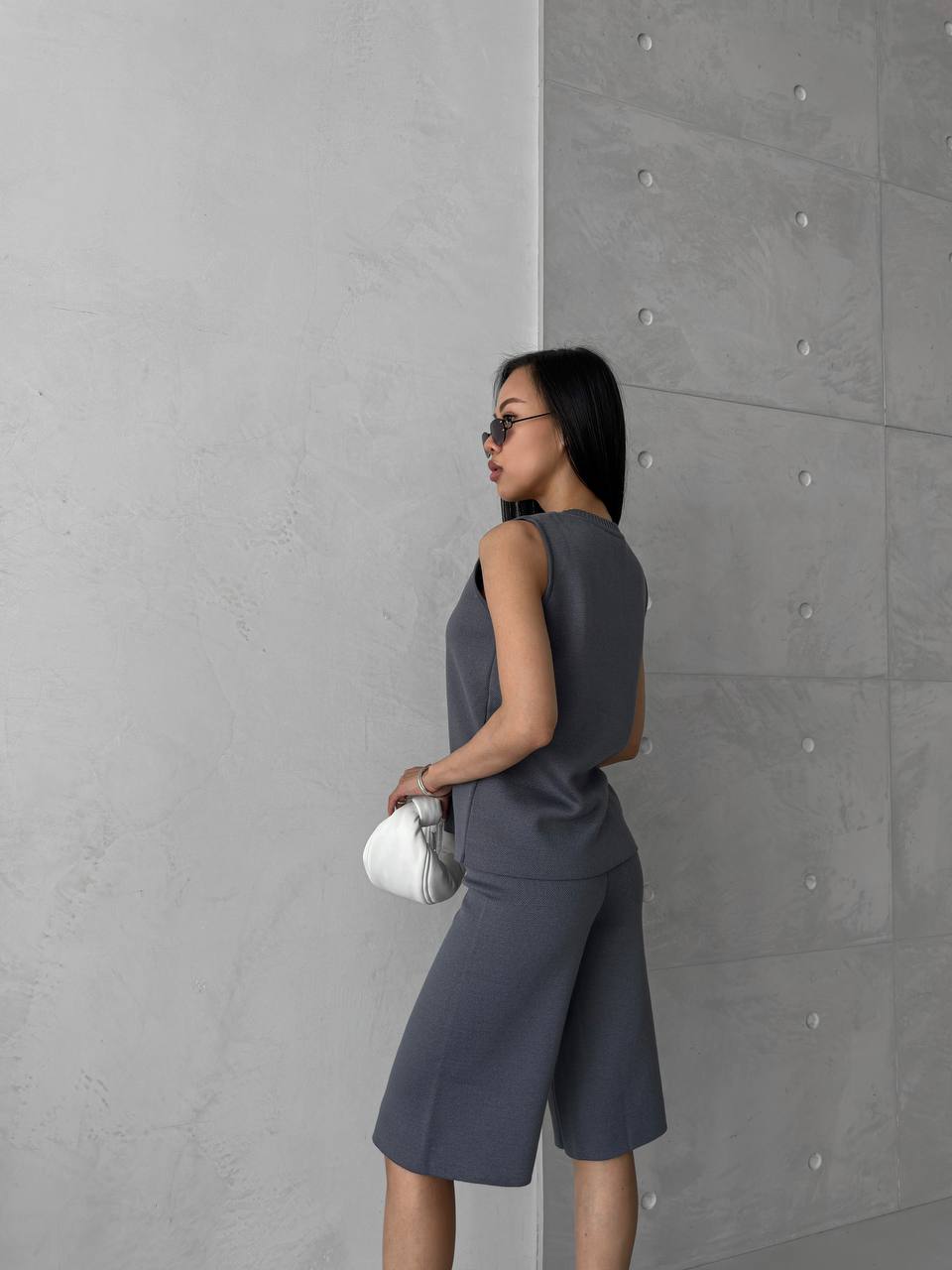 Woman in a gray outfit standing against a gray wall