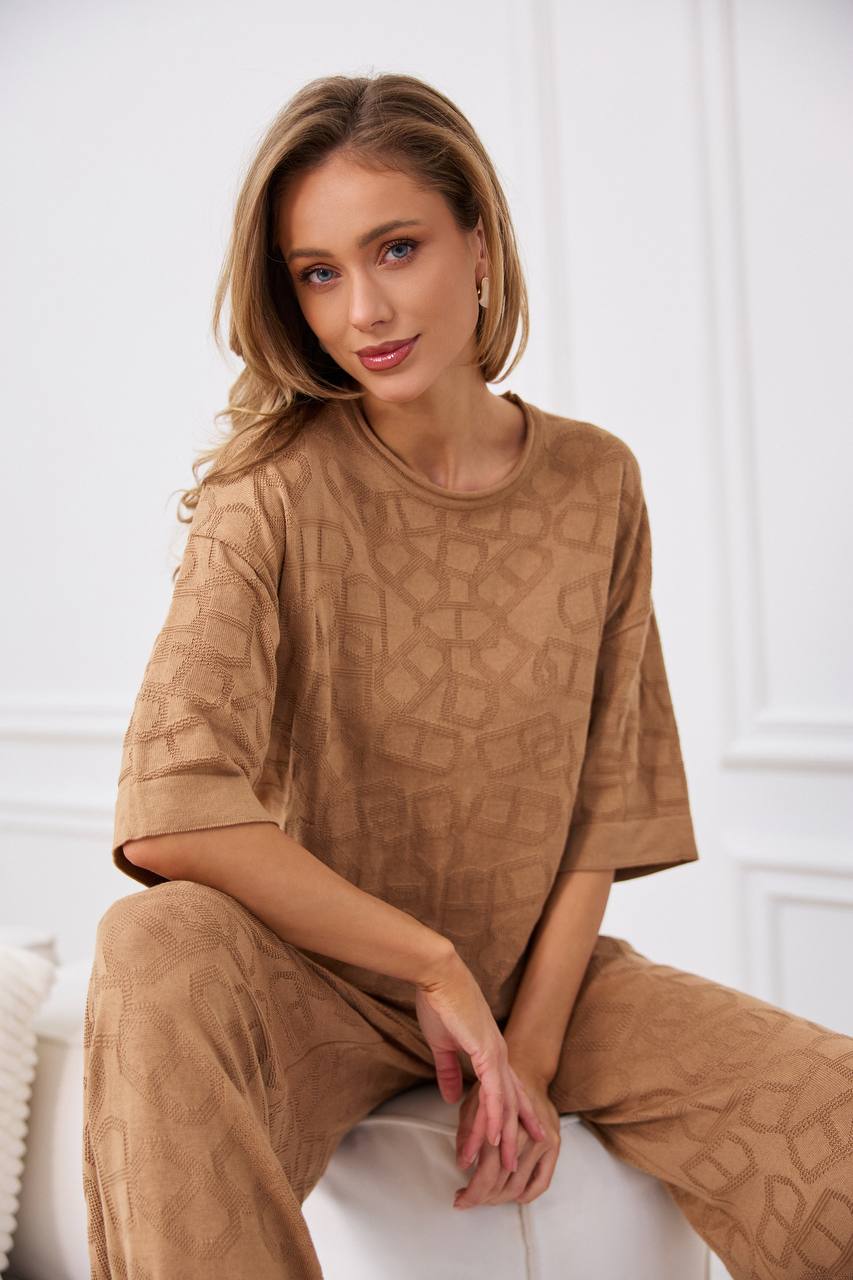 Woman wearing a brown textured outfit sitting on a white surface.