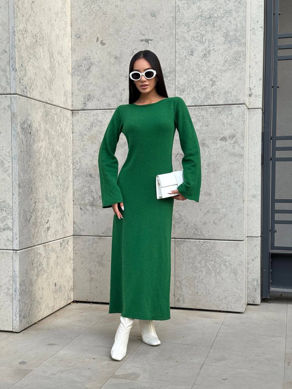 Woman in a green dress standing against a concrete wall.