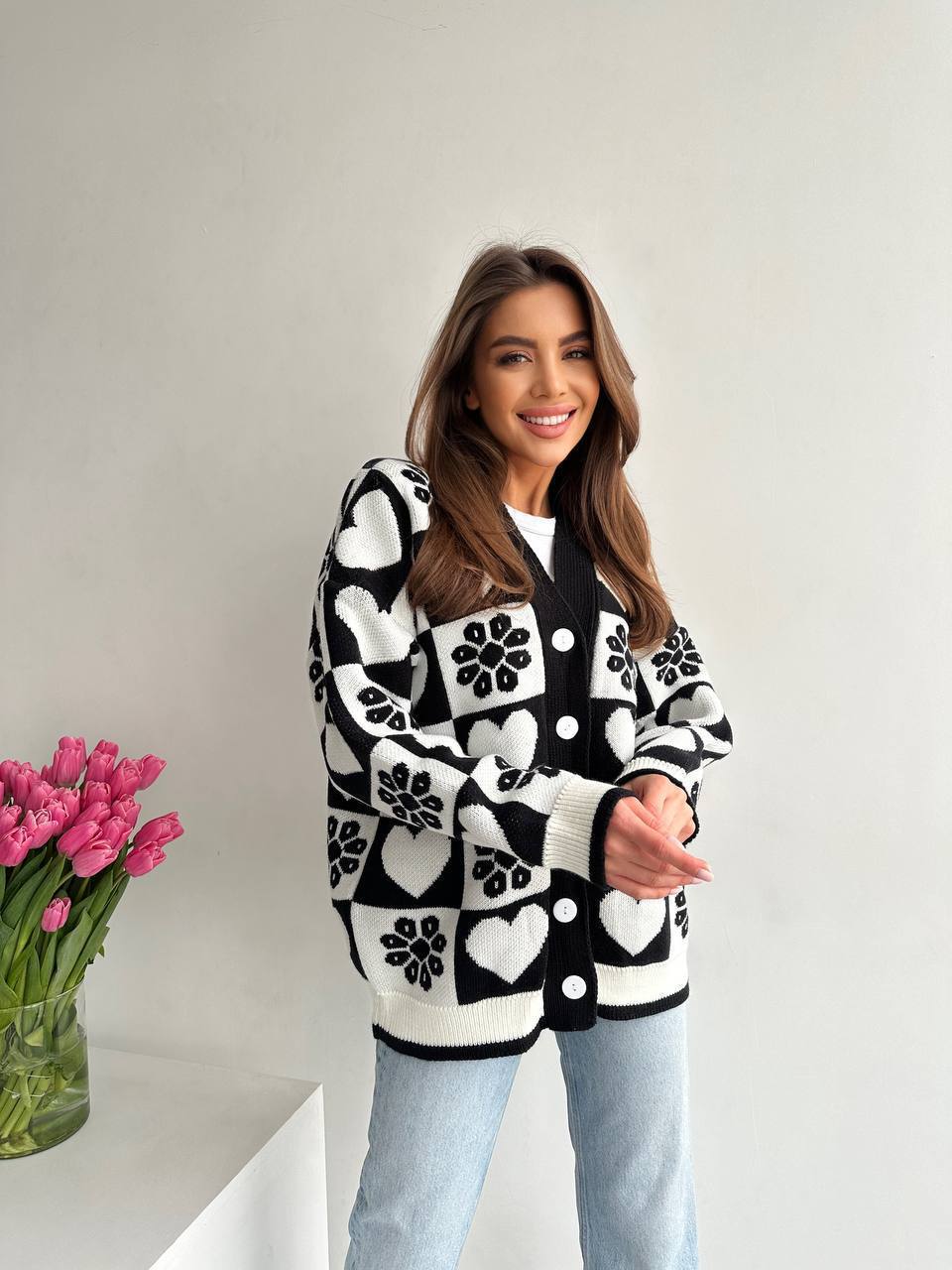 Woman wearing a black and white patterned cardigan with pink tulips in the background