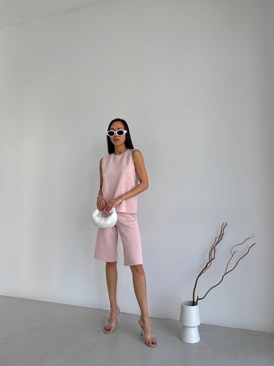 Woman in a pink outfit standing against a plain white wall with minimal decor.