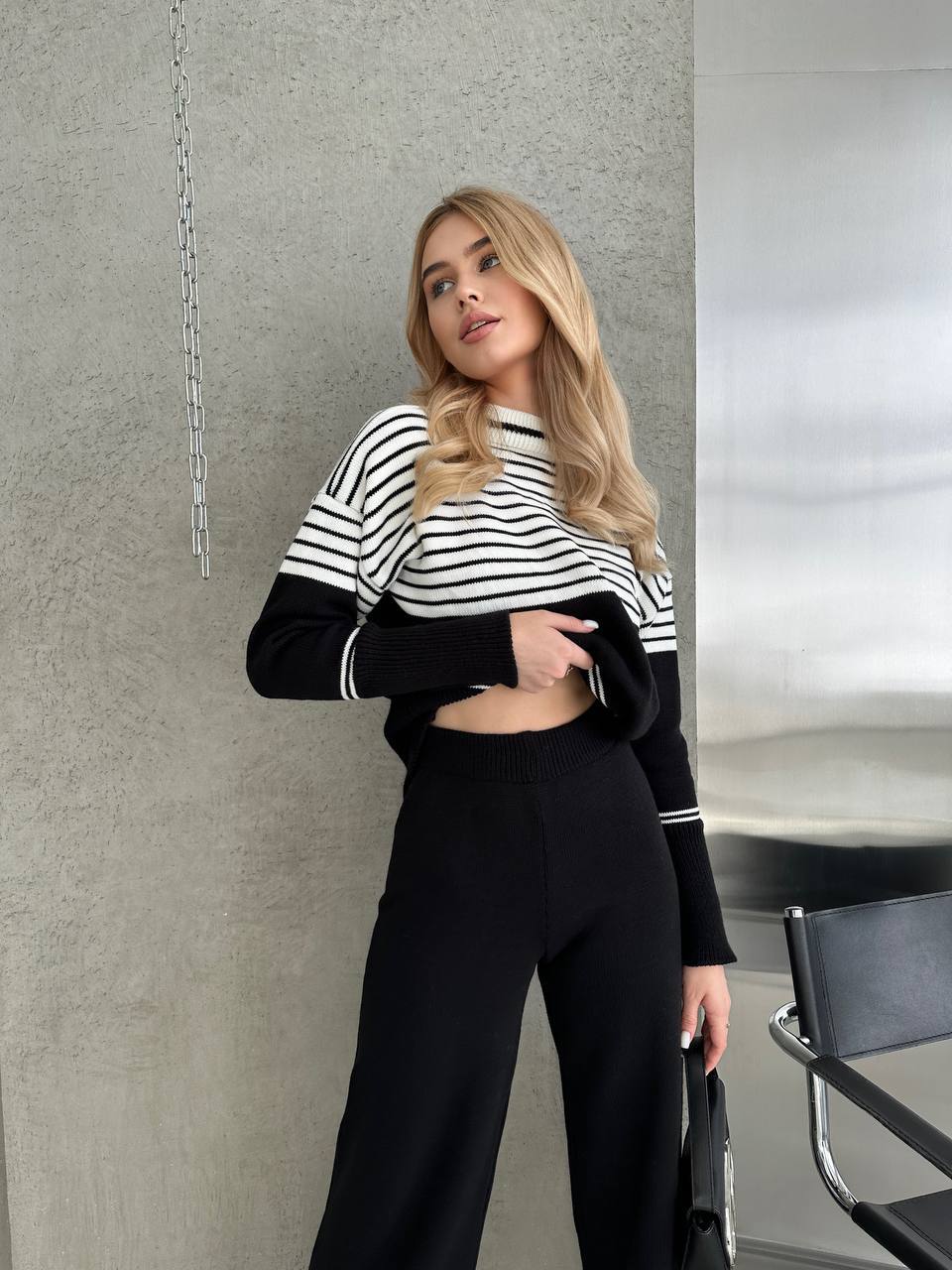 Woman wearing a black and white striped sweater and black pants in an indoor setting.