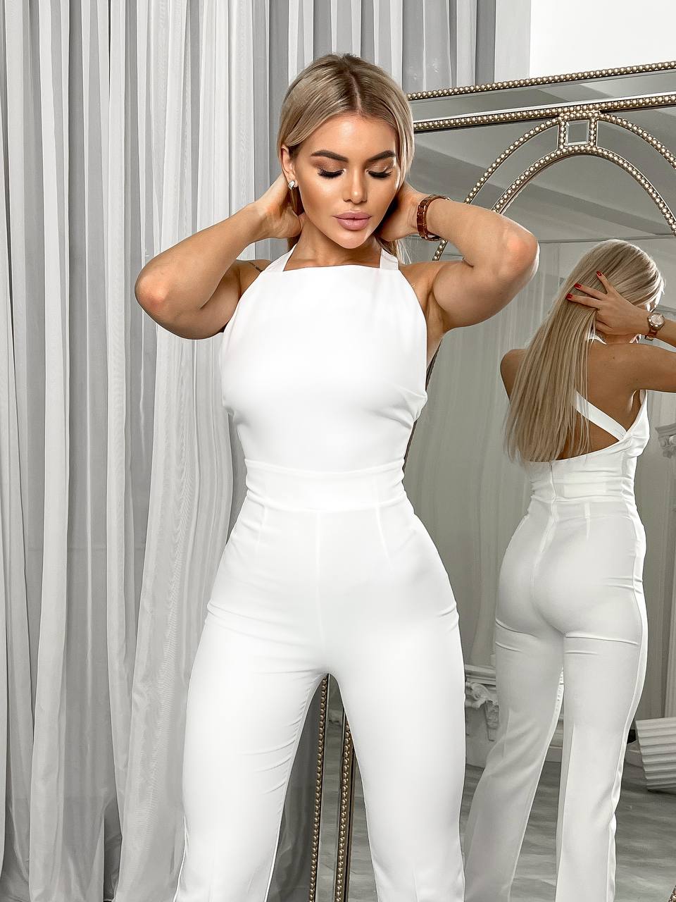 Woman wearing a white jumpsuit standing in front of a mirror.