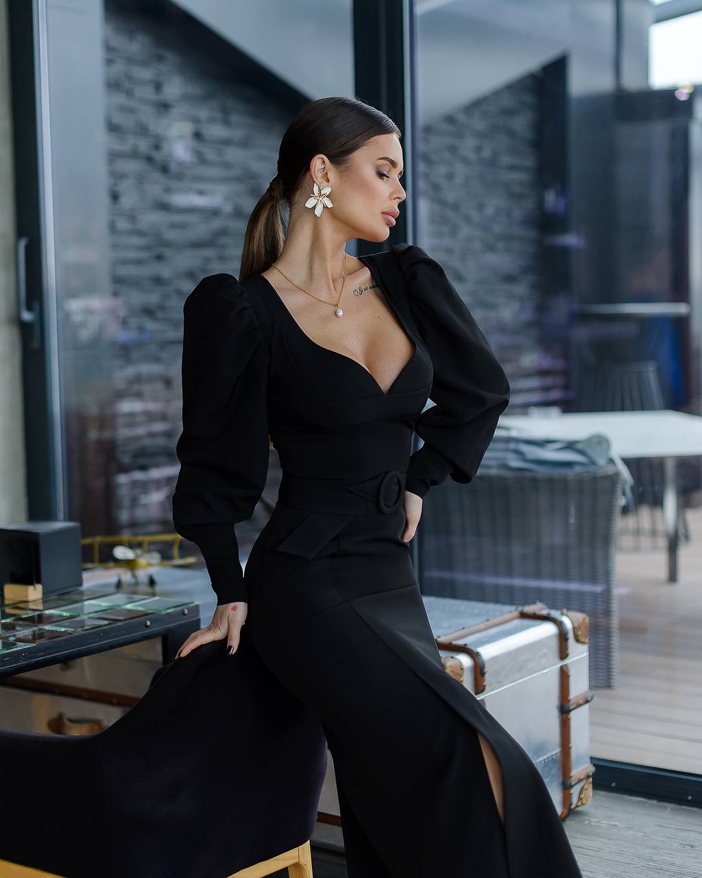 Woman in a black outfit posing in an indoor setting with large windows.