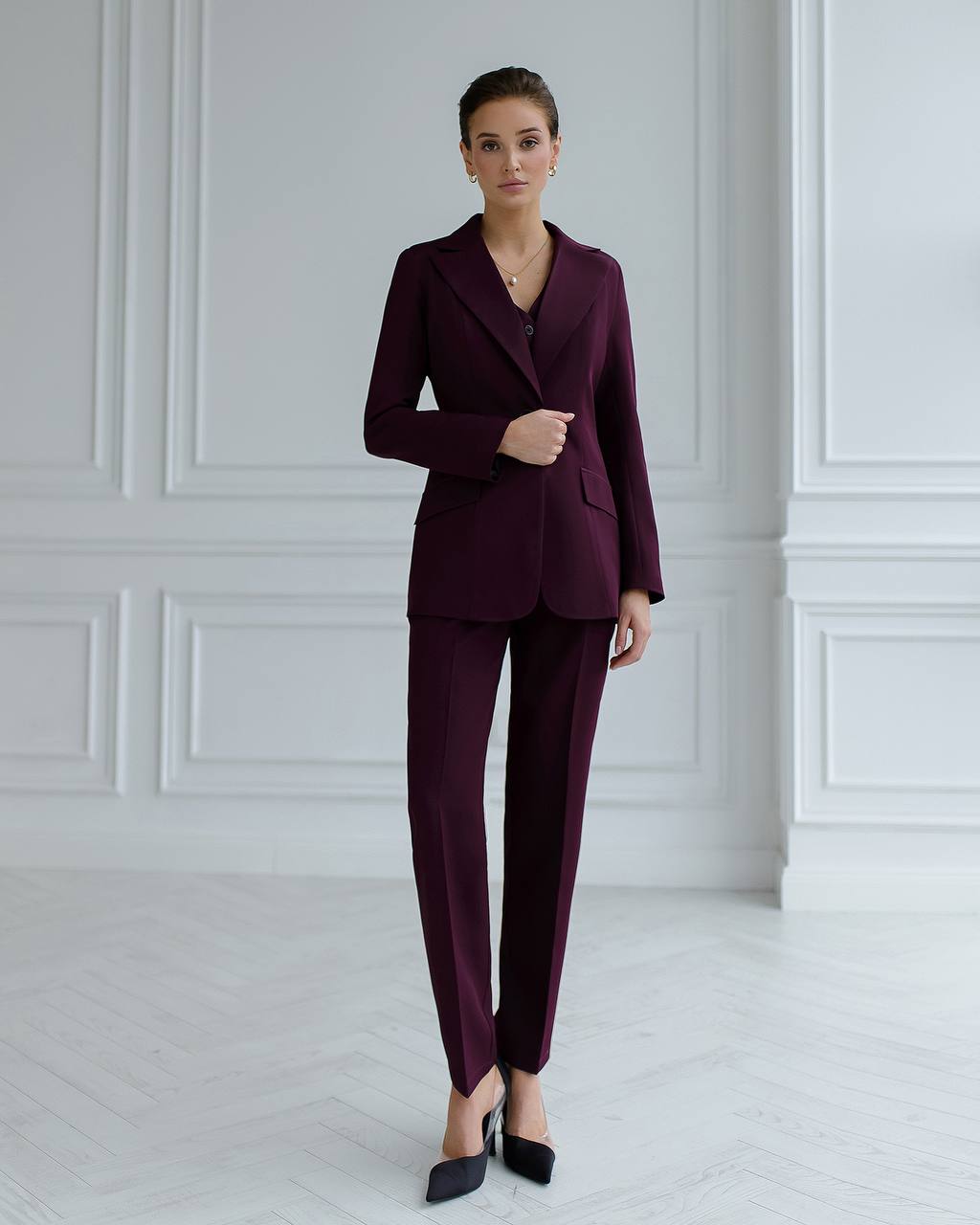 Woman wearing a burgundy suit standing against a white paneled wall.