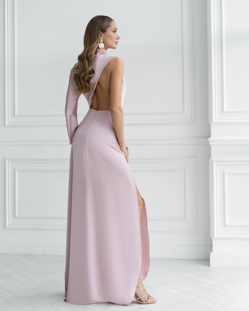 Woman wearing a pink evening gown with a high slit in a white room.