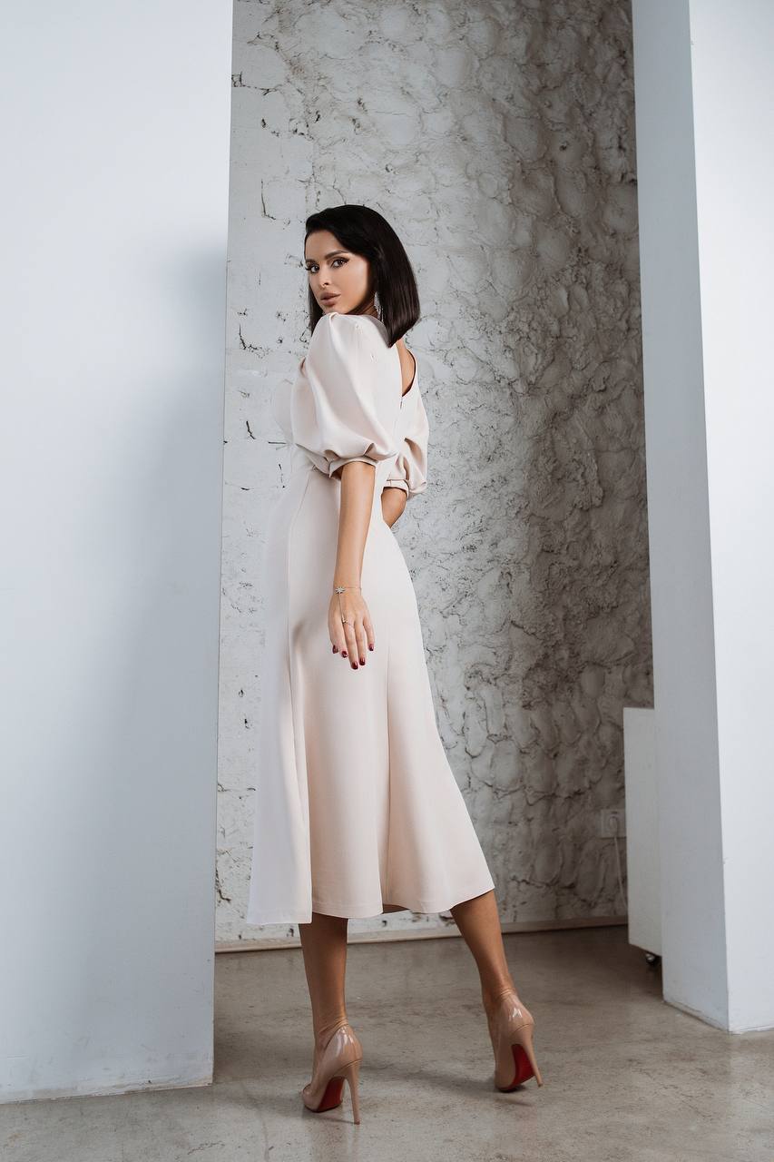 Woman in a white dress standing against a textured wall.