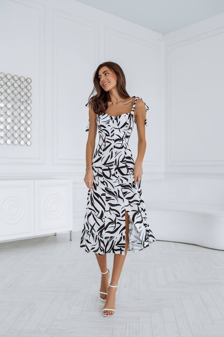 Woman wearing a black and white patterned dress in a minimal white room.