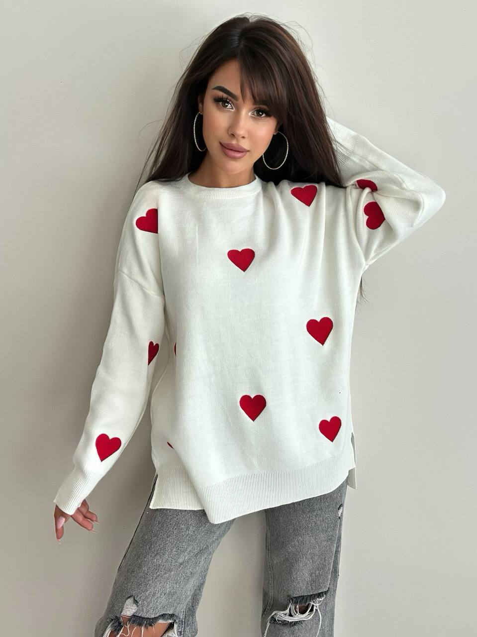 Woman wearing a white sweater with red heart patterns against a plain background