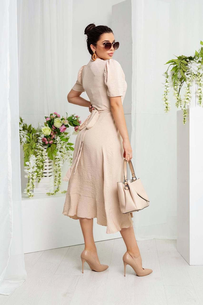 Woman in a beige dress holding a handbag in a minimalistic setting with plants.