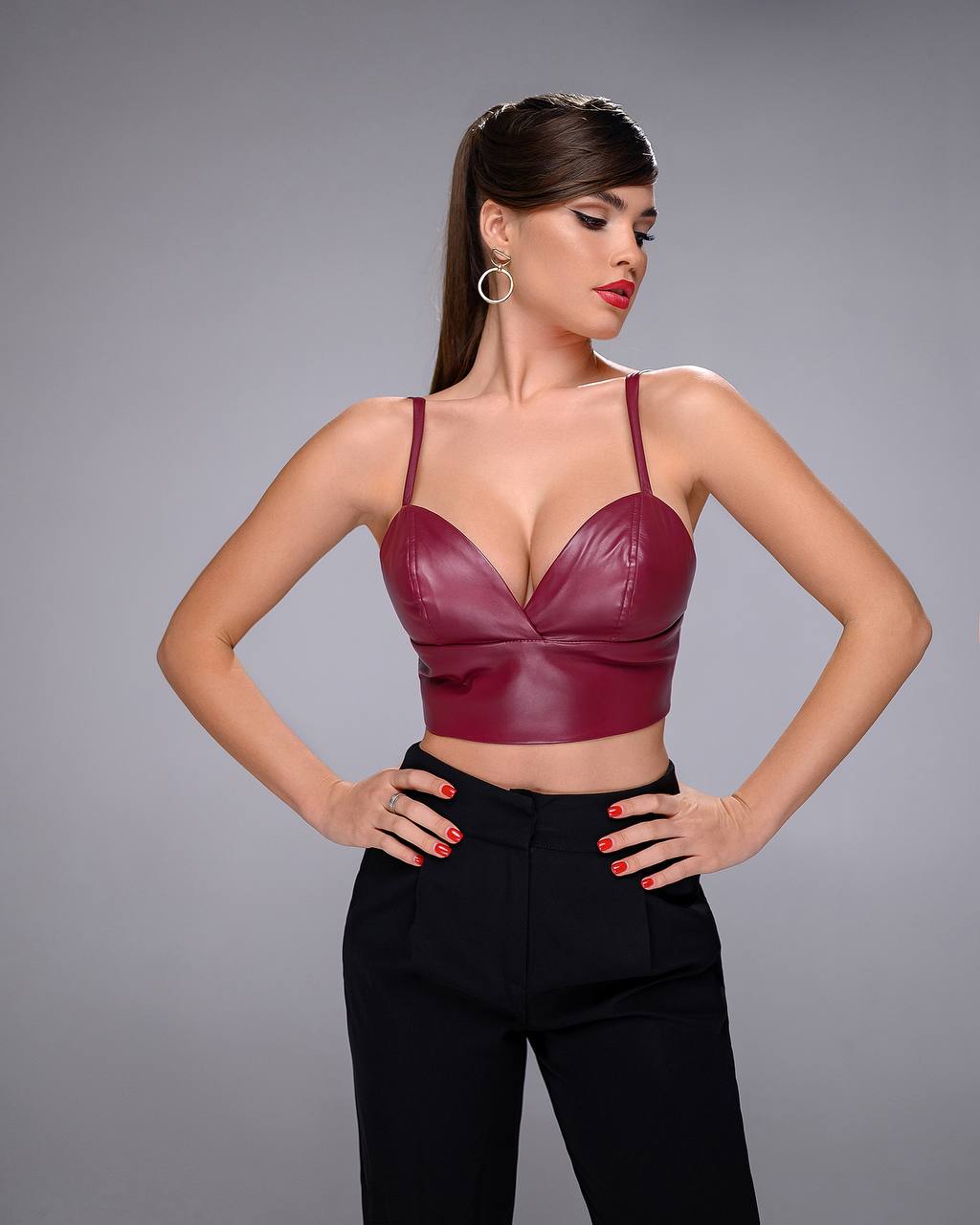 Woman wearing a burgundy leather top and black pants on a gray background