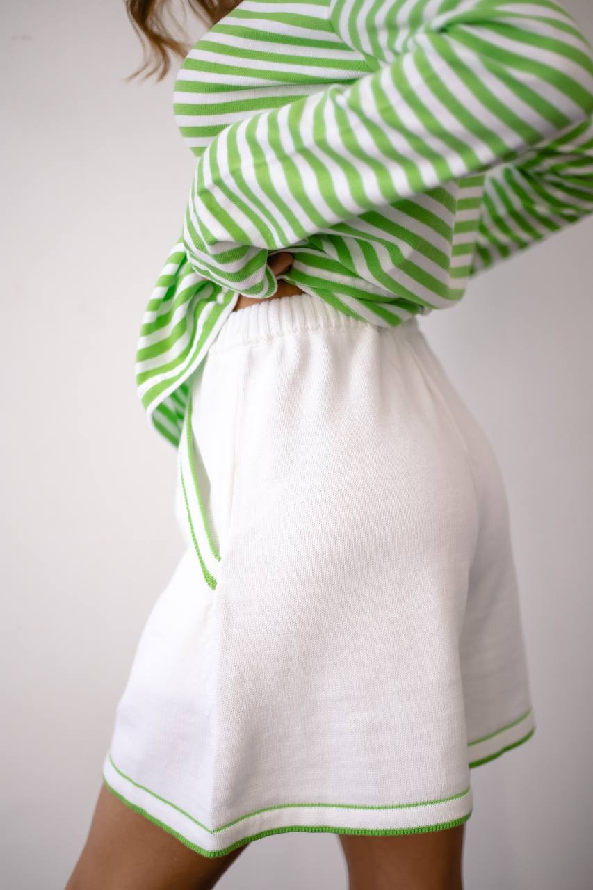 Person wearing a green and white striped sweater with a white skirt on a plain background