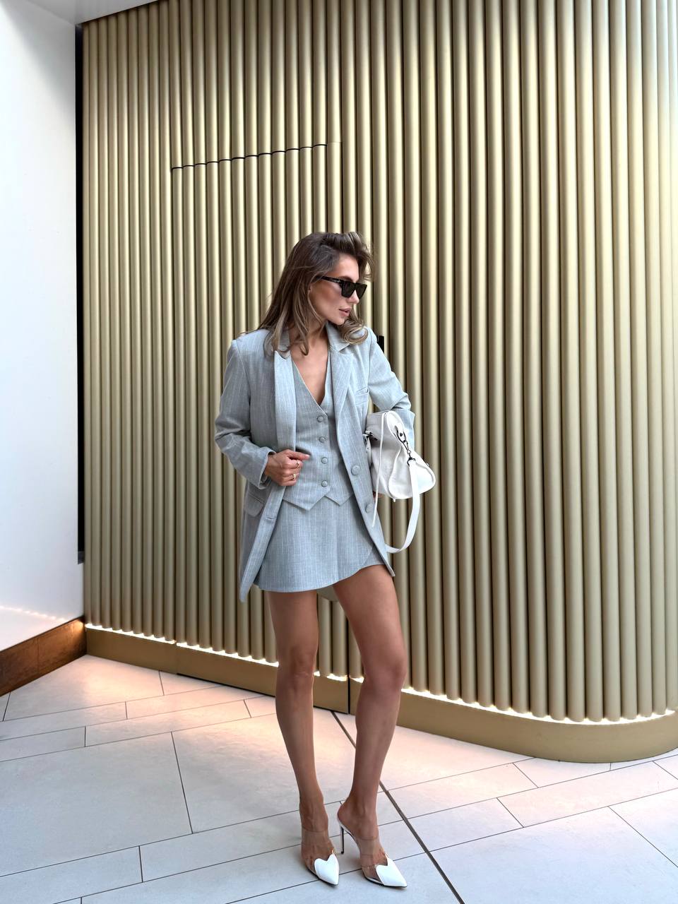 Woman in a stylish outfit standing against a modern wall.