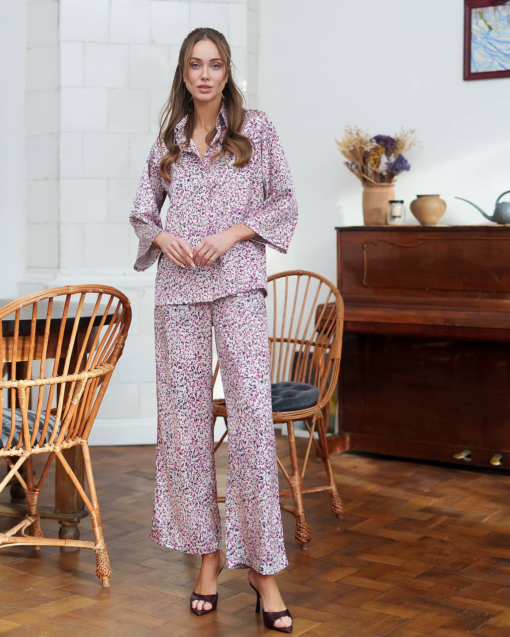 Woman in a floral pajama set standing in a room with wooden furniture and a piano.