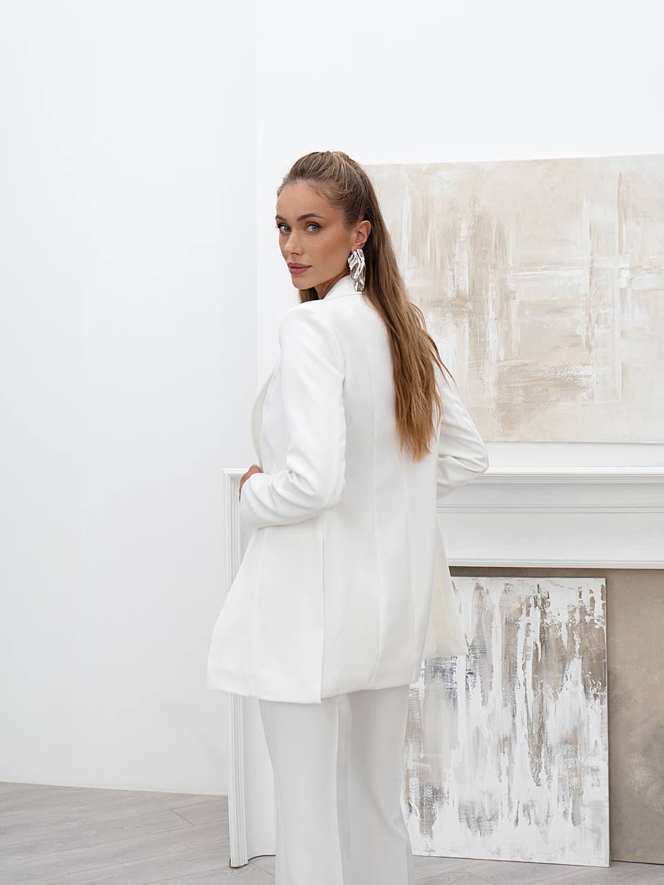 Woman in a white outfit standing in a minimalistic room with abstract art on the wall.
