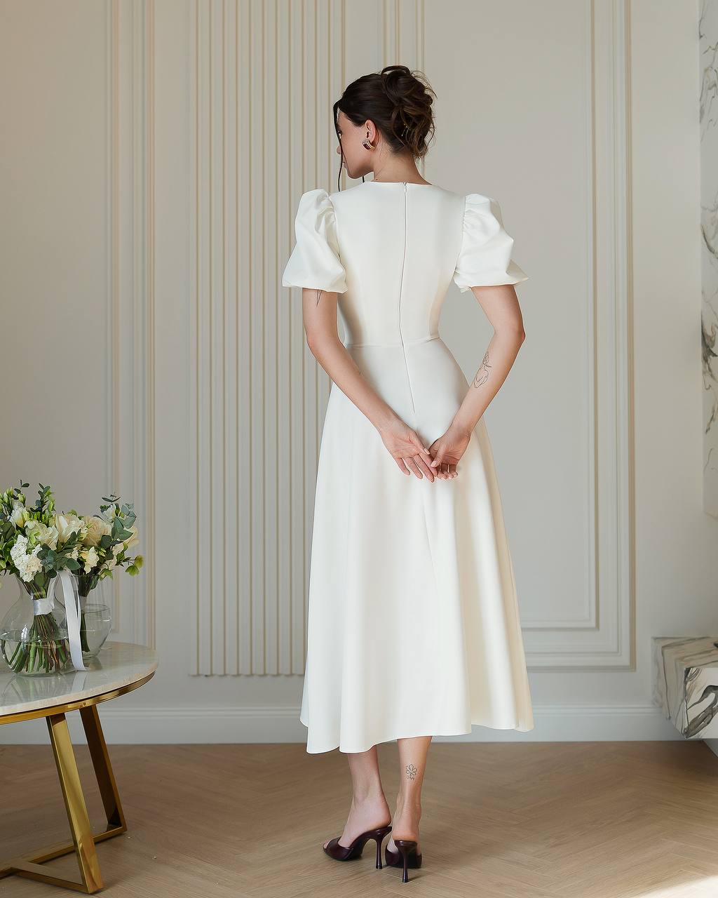 Woman wearing a white dress standing in a room with decorative wall paneling.