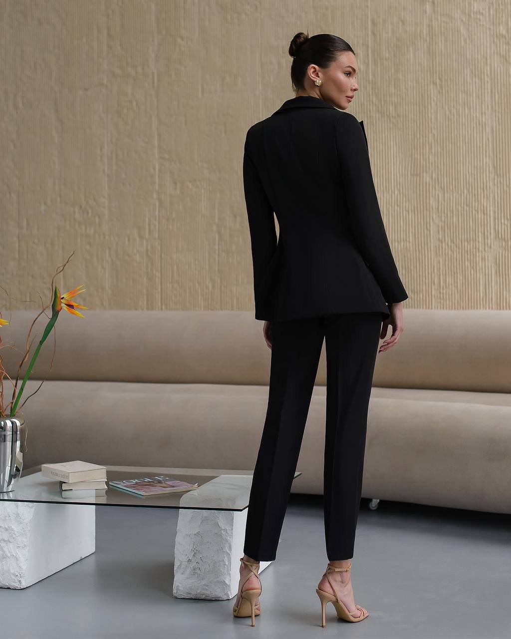 Woman in a black suit standing in a modern living room.