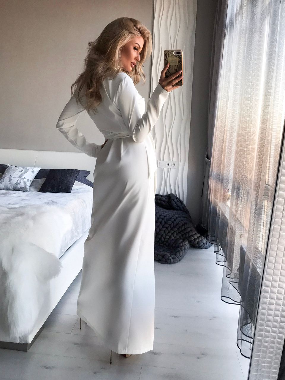 Woman in a white robe taking a mirror selfie in a bedroom.