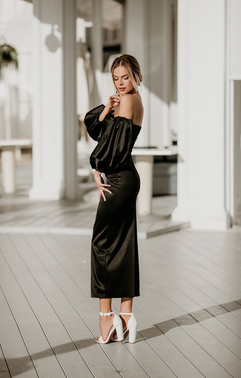 Woman in a black off-shoulder dress standing on a wooden deck.