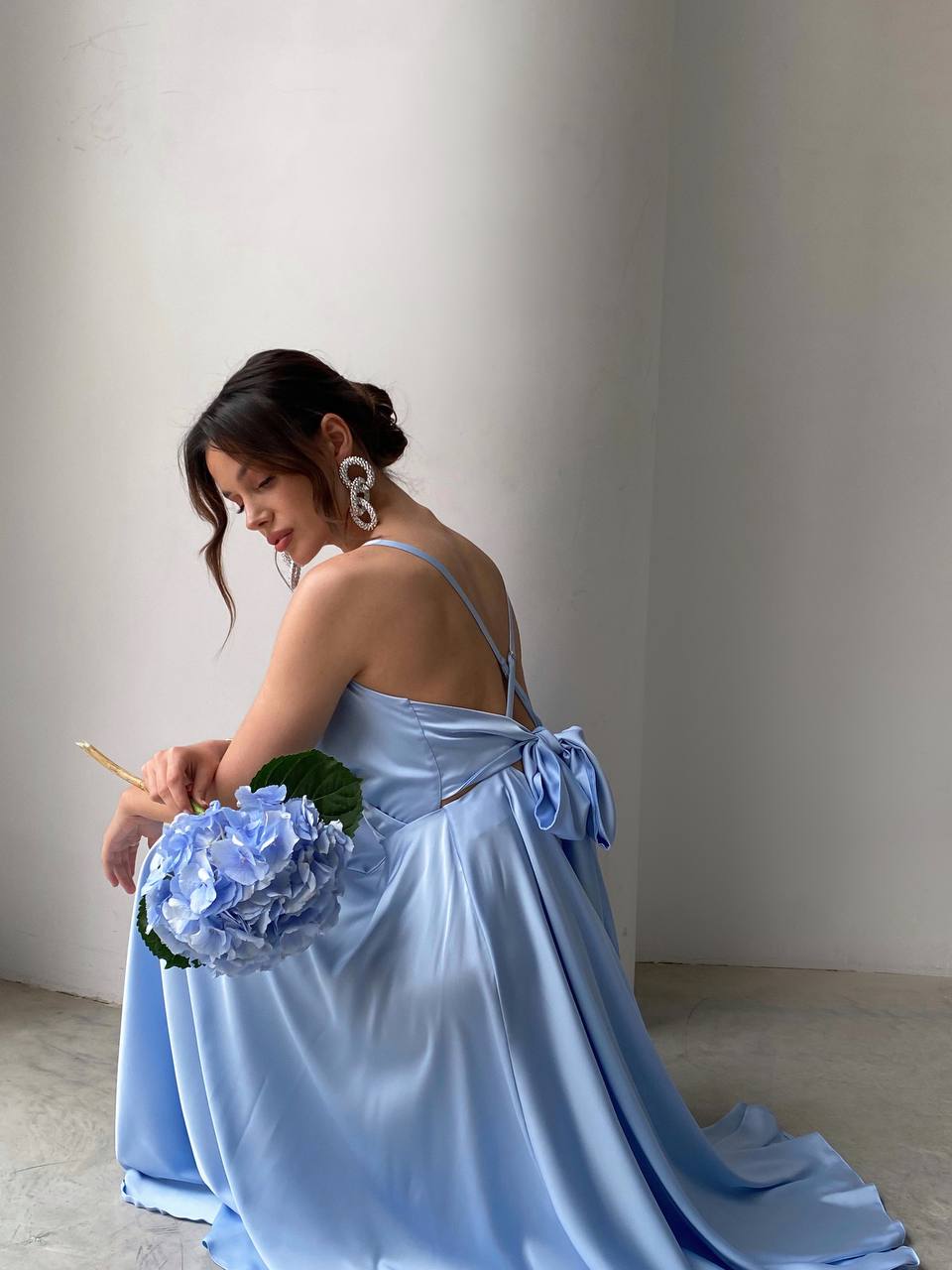 Woman in a light blue dress holding flowers against a plain background