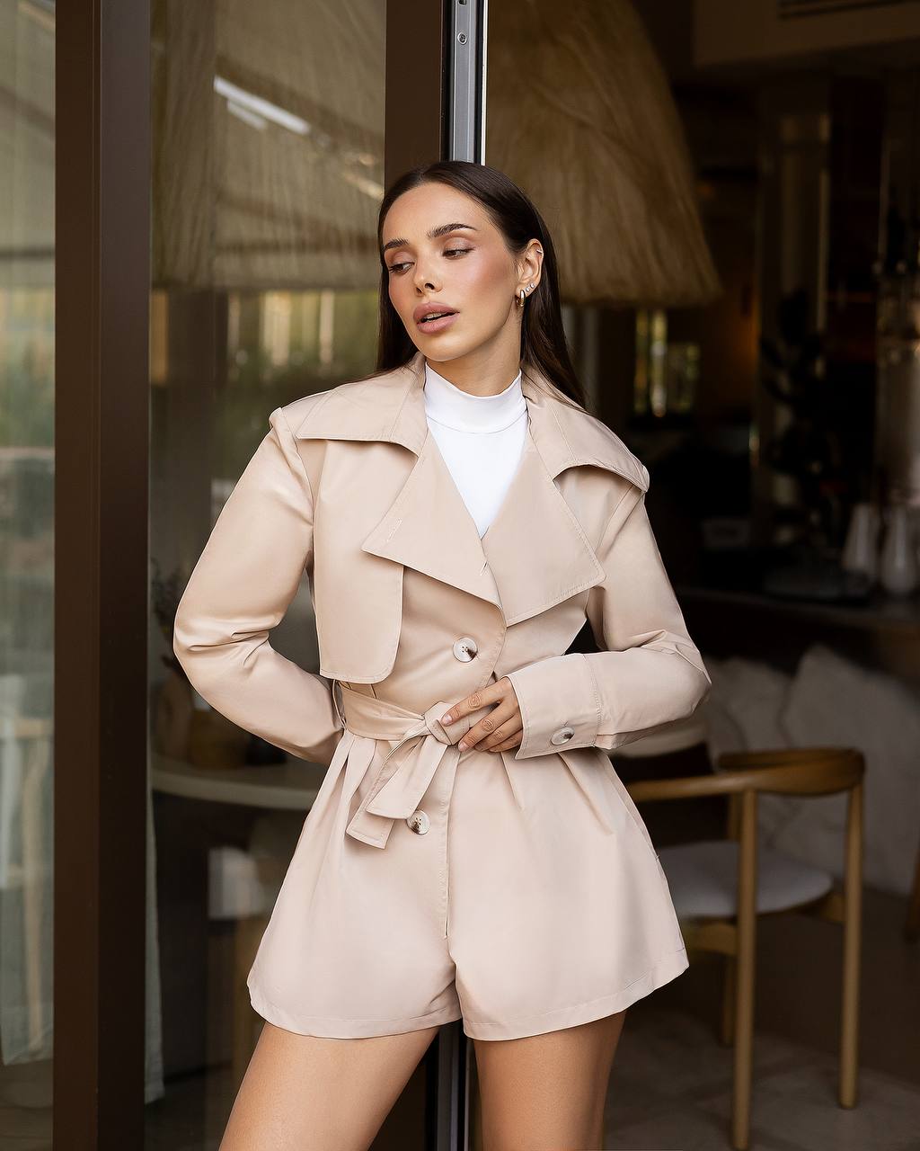 Woman wearing a beige trench coat and shorts in an indoor setting