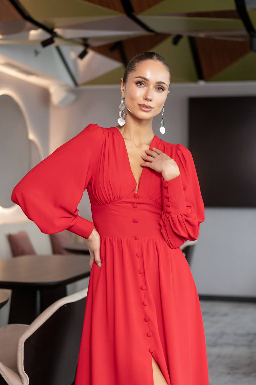 Woman in a red dress posing in an indoor setting with tables and chairs.