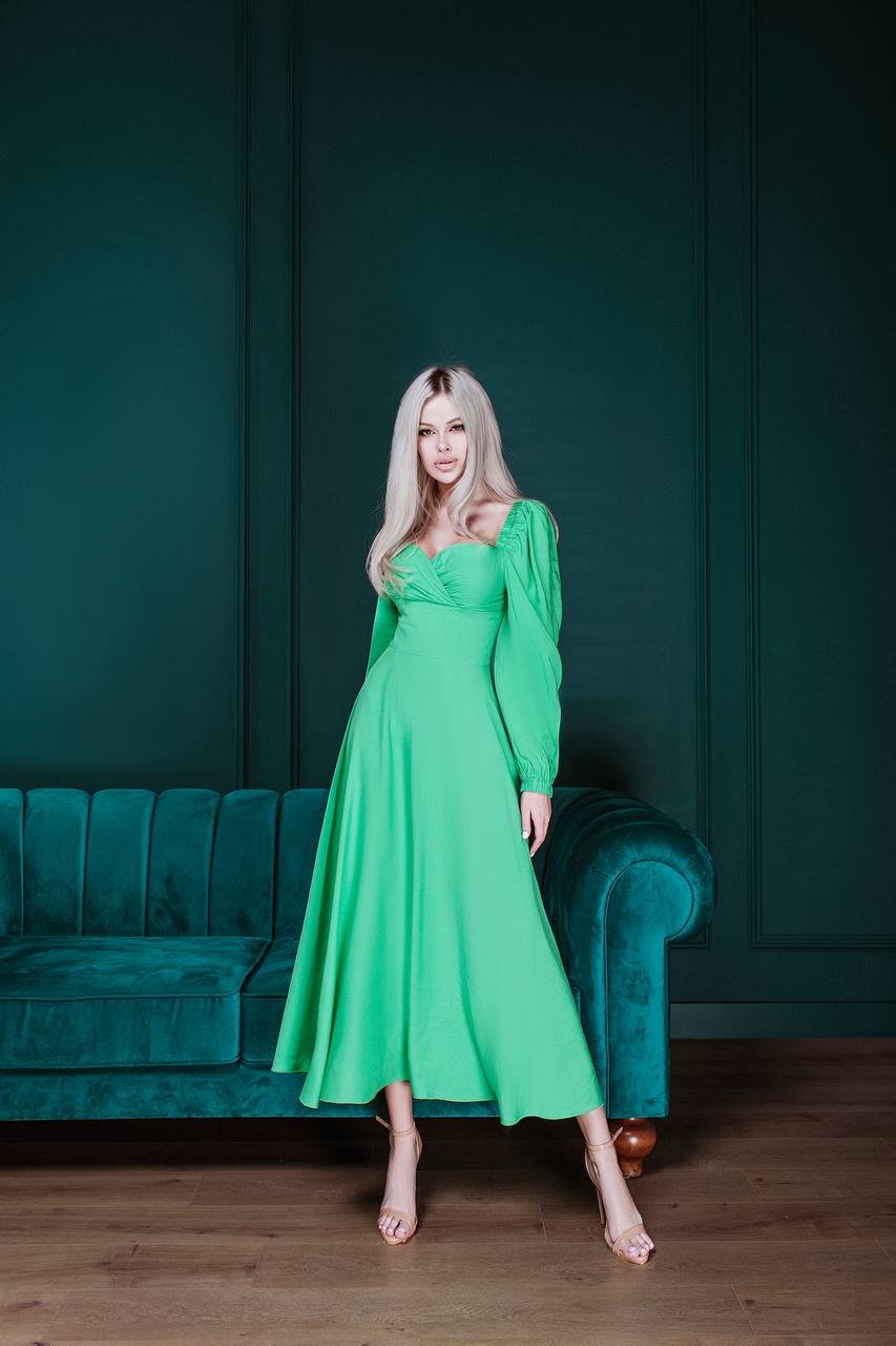 Woman in a green dress standing in a room with teal walls and a teal couch.