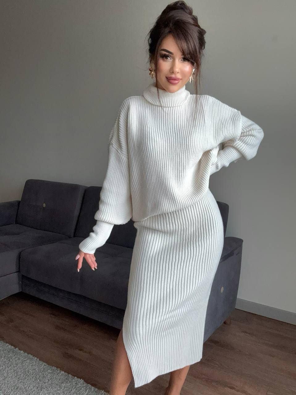 Woman wearing a white ribbed knit outfit in a room with a gray sofa.