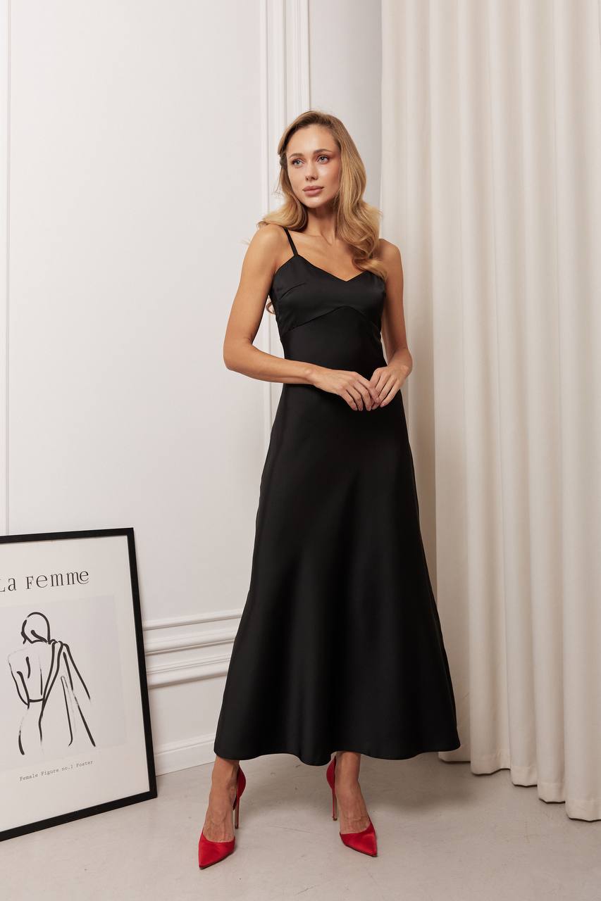 Woman wearing a black dress with red shoes standing in a room with white curtains and a framed picture on the wall.