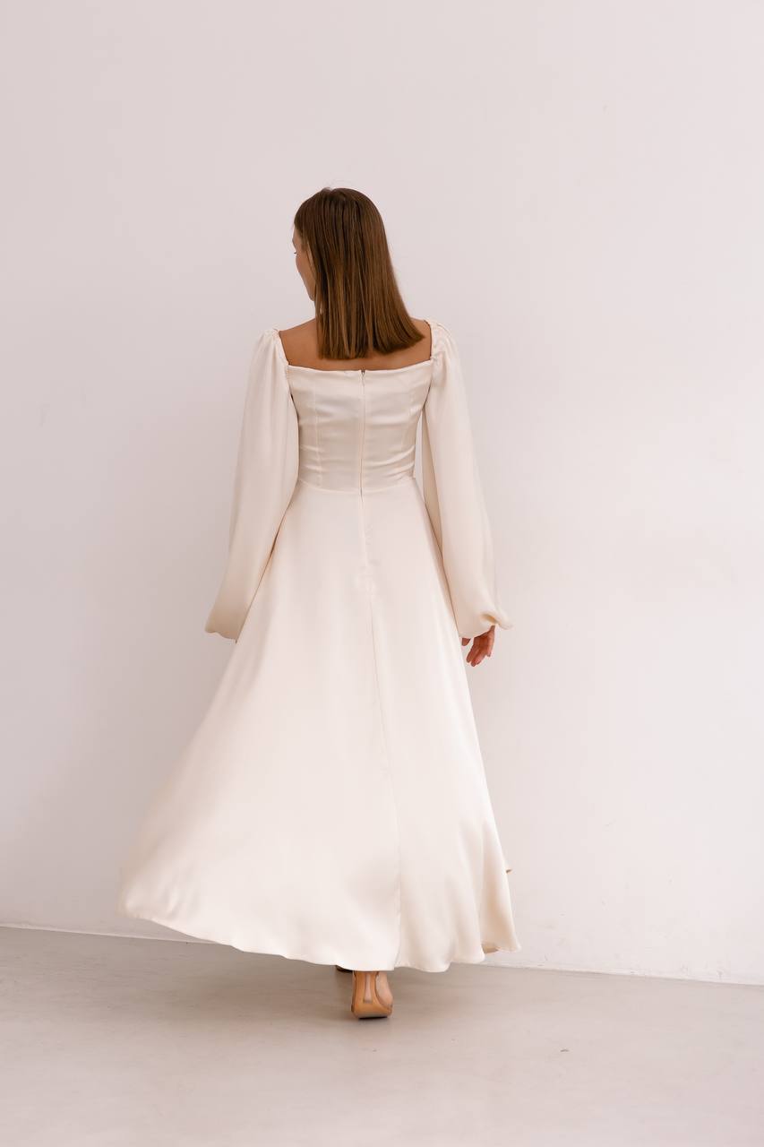 Woman wearing a long, light-colored dress with long sleeves against a plain white background