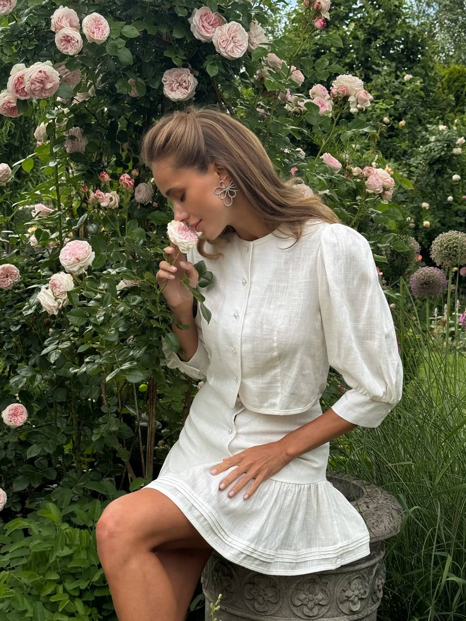 Woman in a white dress smelling flowers in a garden