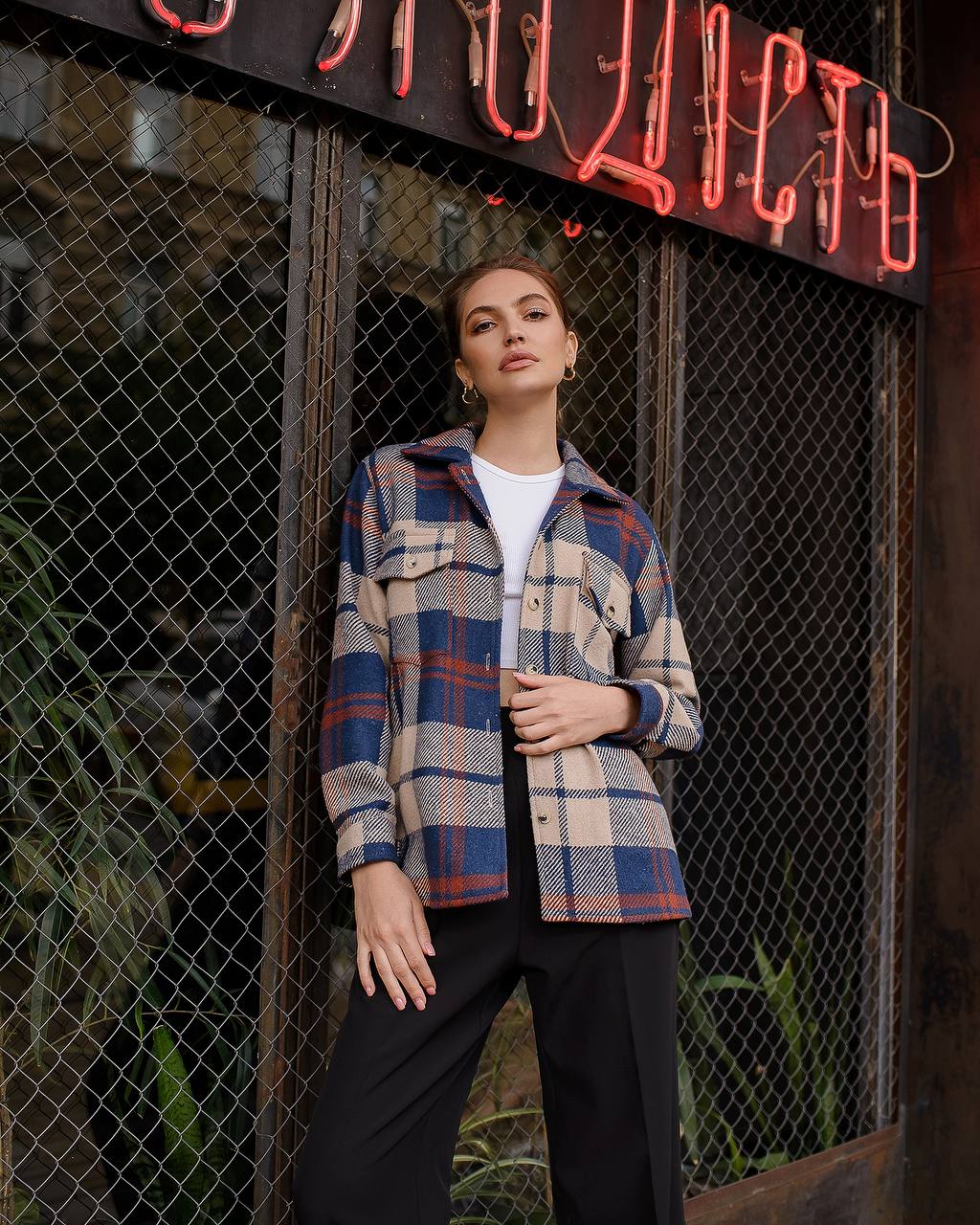 Person wearing a plaid shirt standing in front of a neon sign