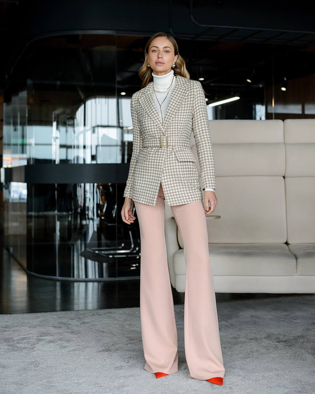 Woman in a checkered blazer and pink pants standing in an indoor setting.