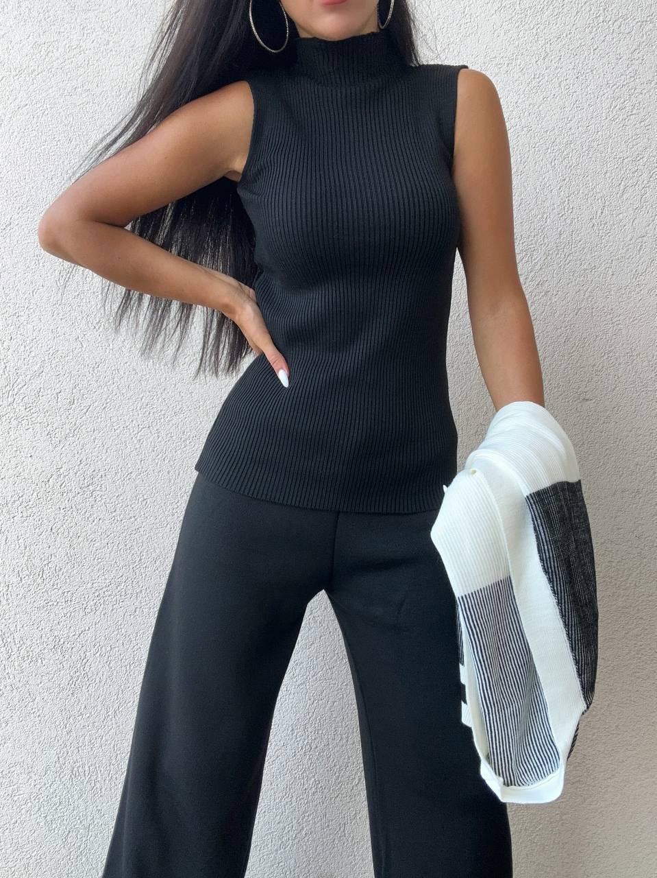 Person wearing a black sleeveless top and black pants against a light background