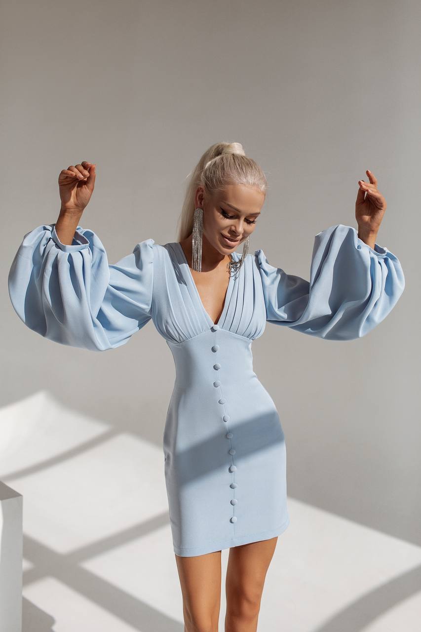 Woman wearing a light blue dress with puffed sleeves in a well-lit room.