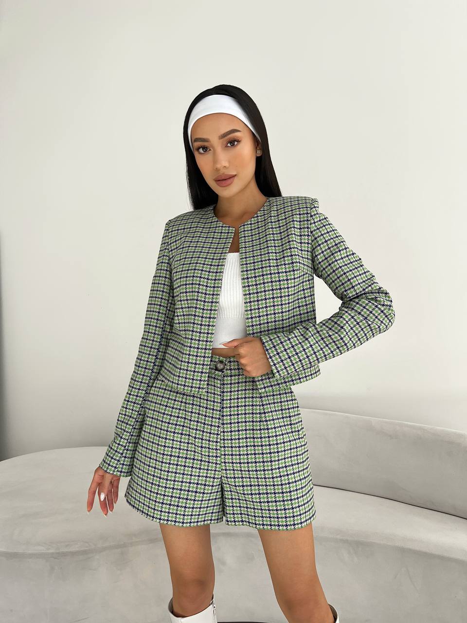 Woman wearing a green plaid suit with a white top and headband on a neutral background