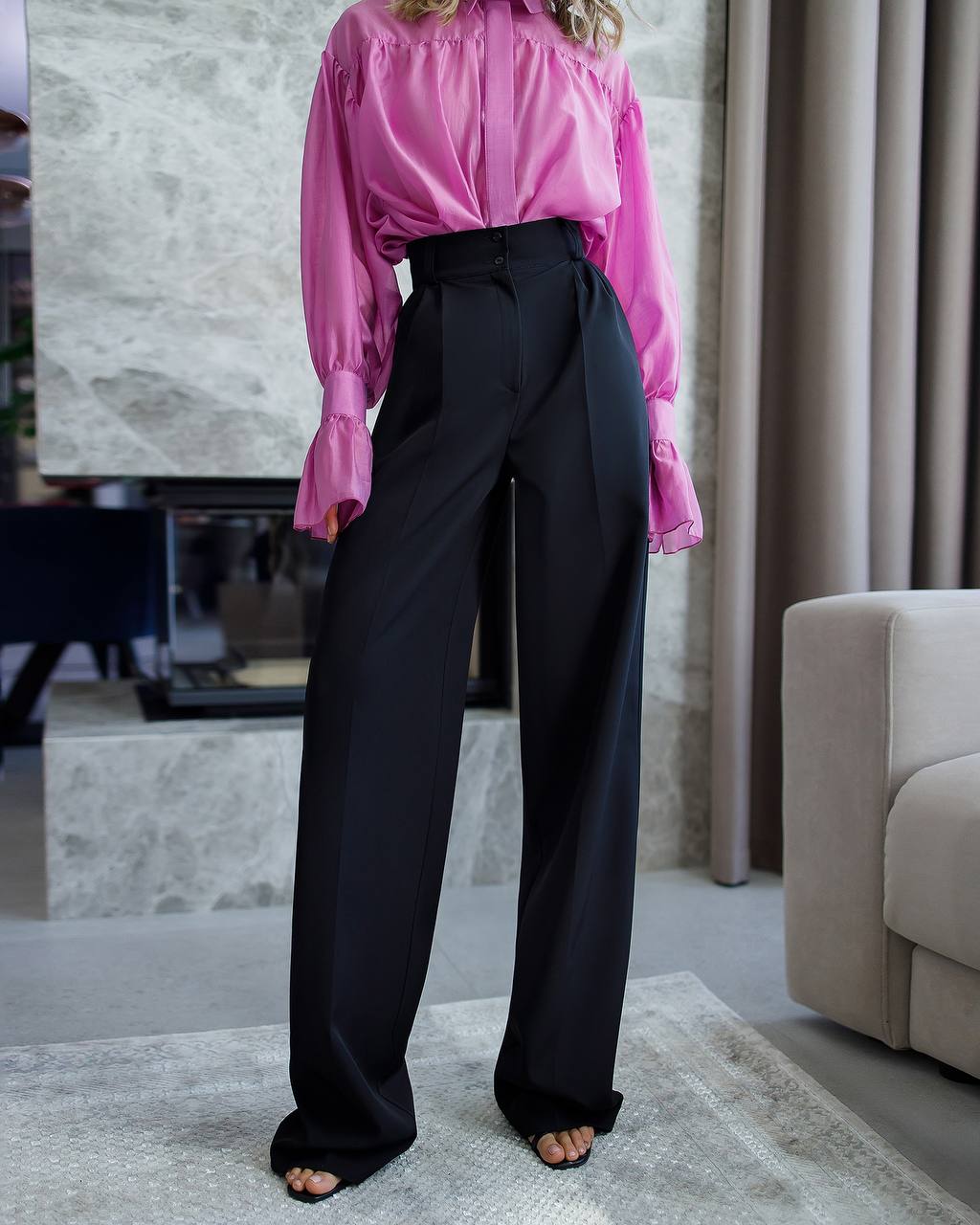 Person wearing a pink blouse and black pants in an indoor setting