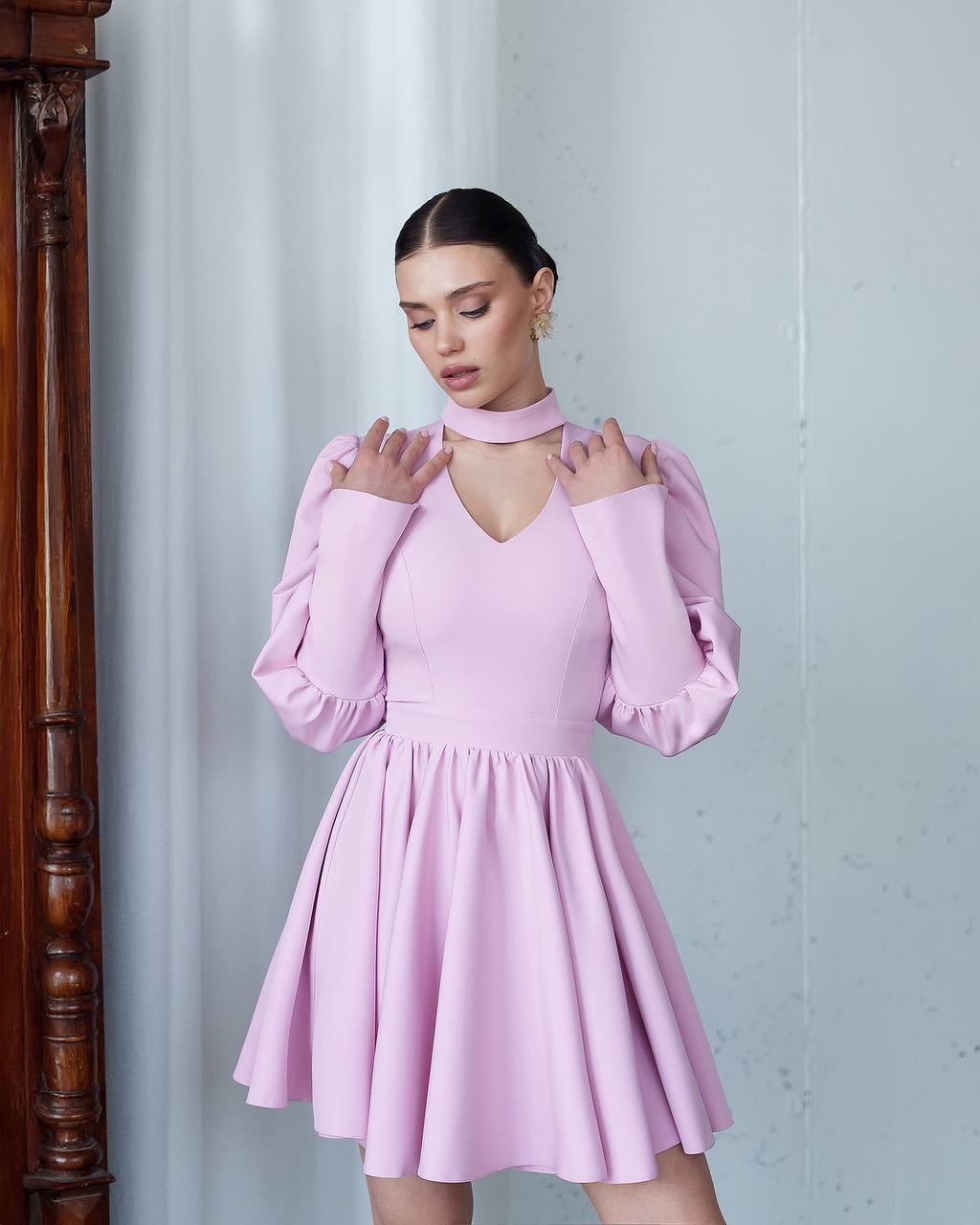 Woman wearing a pink dress with long sleeves against a light gray wall.