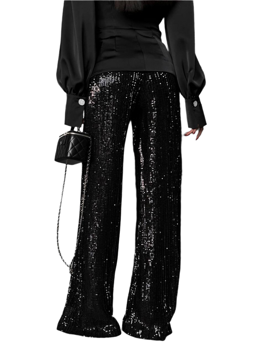 Person wearing black sequin pants with a black top and handbag on a white background
